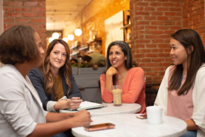 Image shows four women sitting around table talking and smiling