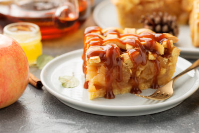 Slice of apple pie with caramel sauce on a white plate.