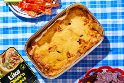 Yummy vegan Super Bowl recipes: a pan of buffalo chicken dip is accompanied by a plate of veggies and tortilla chips on a bright blue gingham table cloth